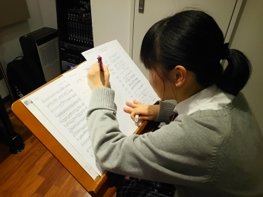譜面台に置かれた楽譜に書き込みする生徒