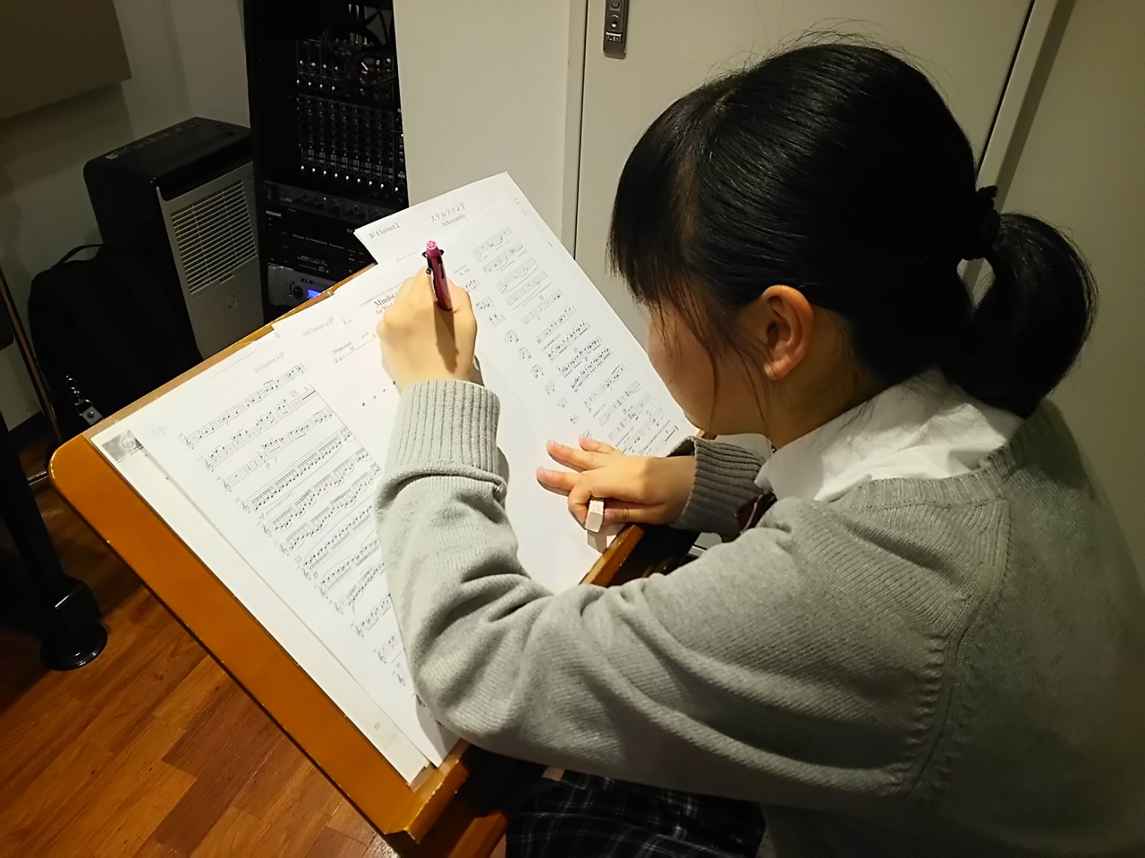 譜面台に置かれた楽譜に書き込みする生徒